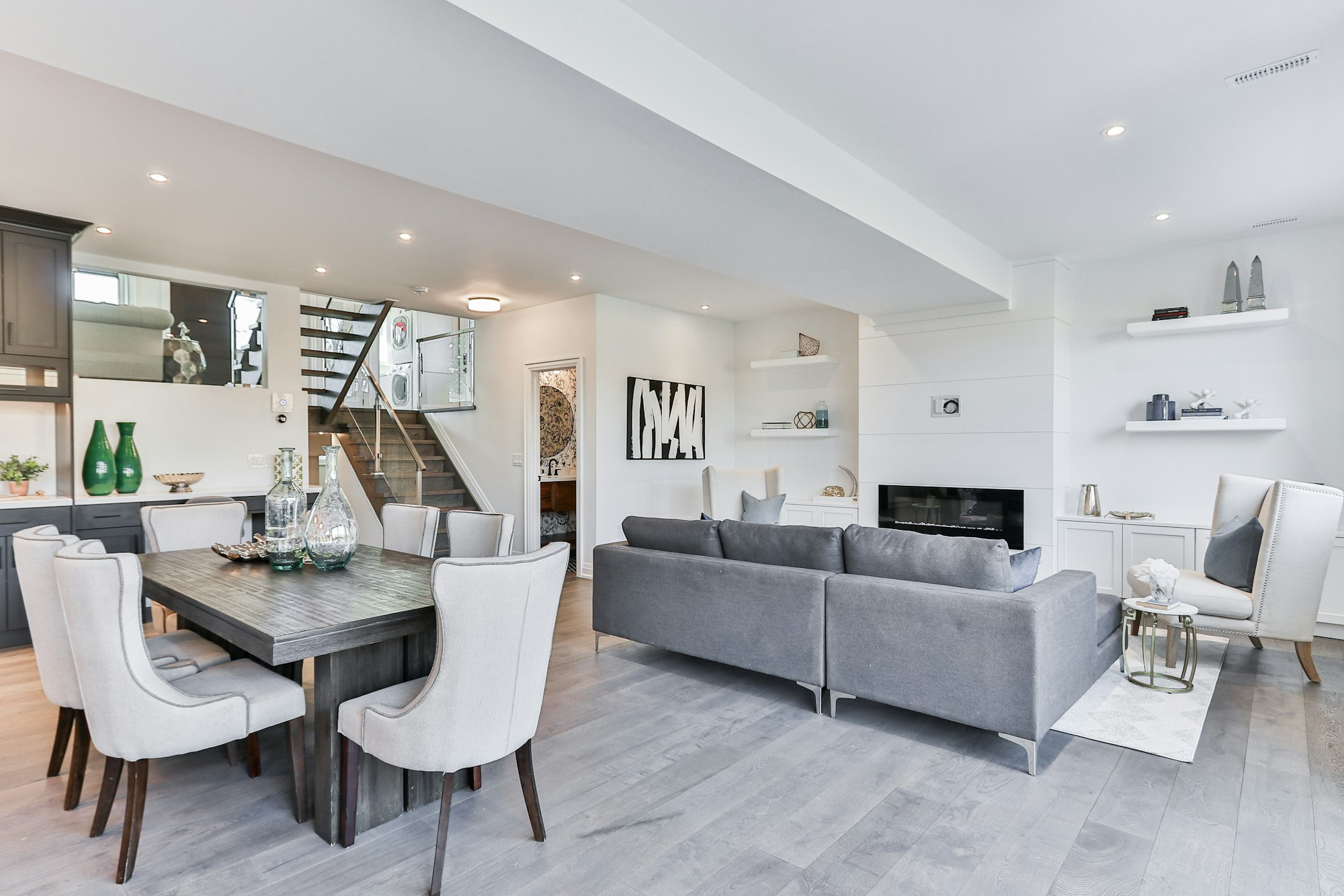 Planta abierta con comedor de sillas tapizadas en blanco, sofá gris y chimenea al fondo