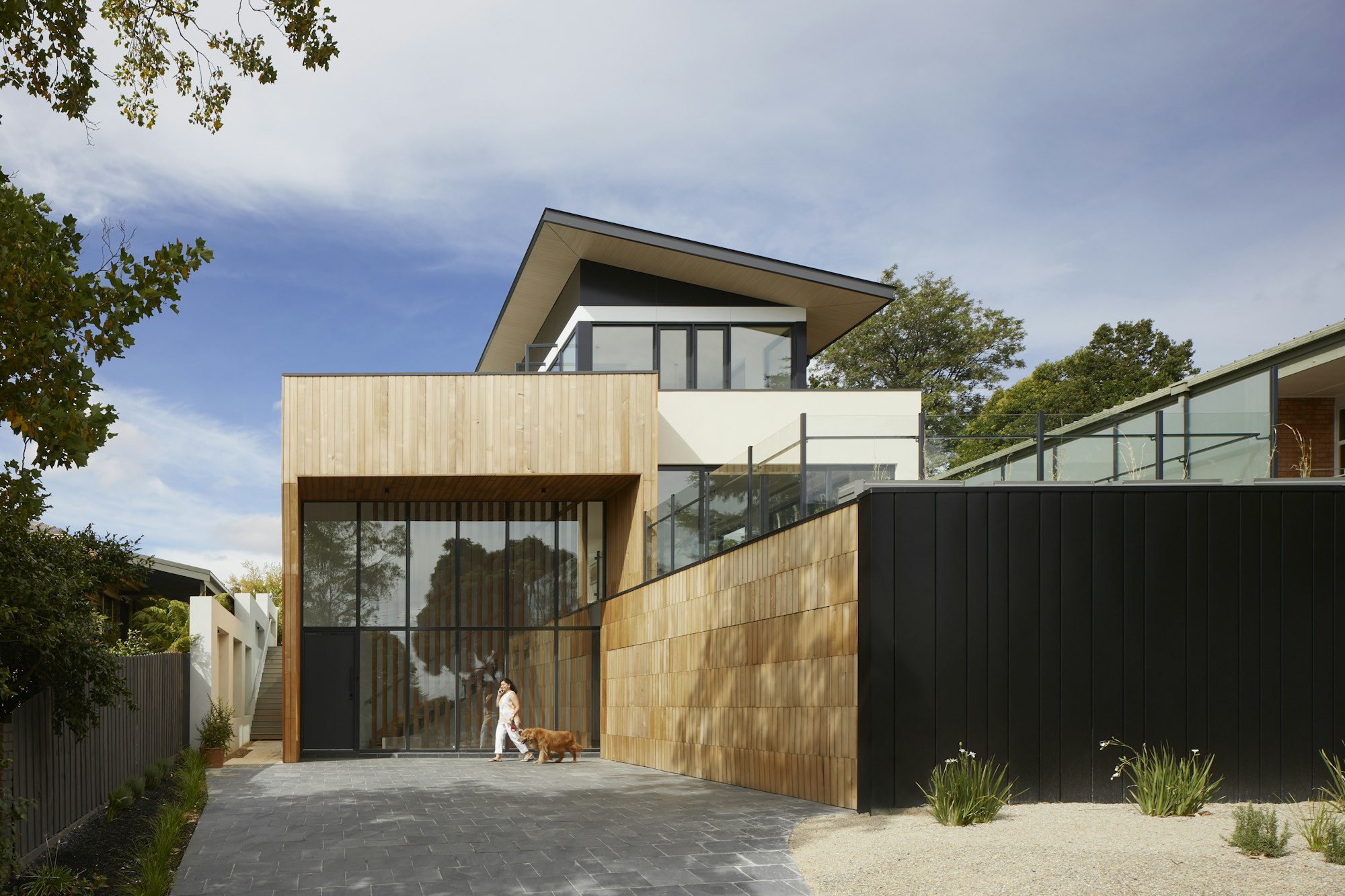 Fachada de madera y paneles negros con un gran ventanal sobre la entrada